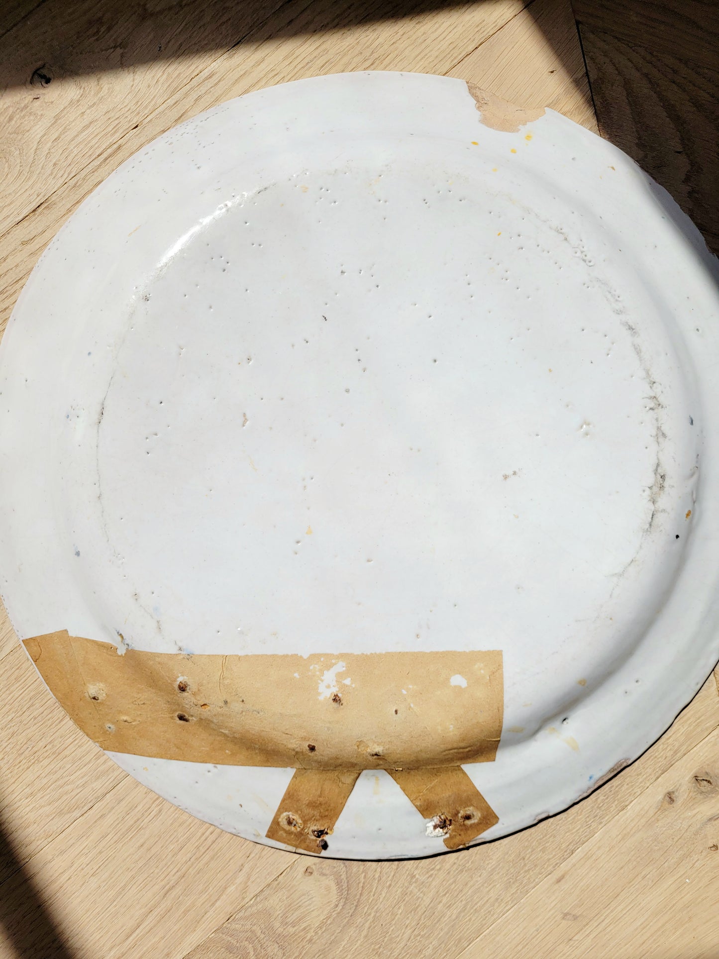 back view of a large hand-painted wall plate with rural landscape on a parquet 