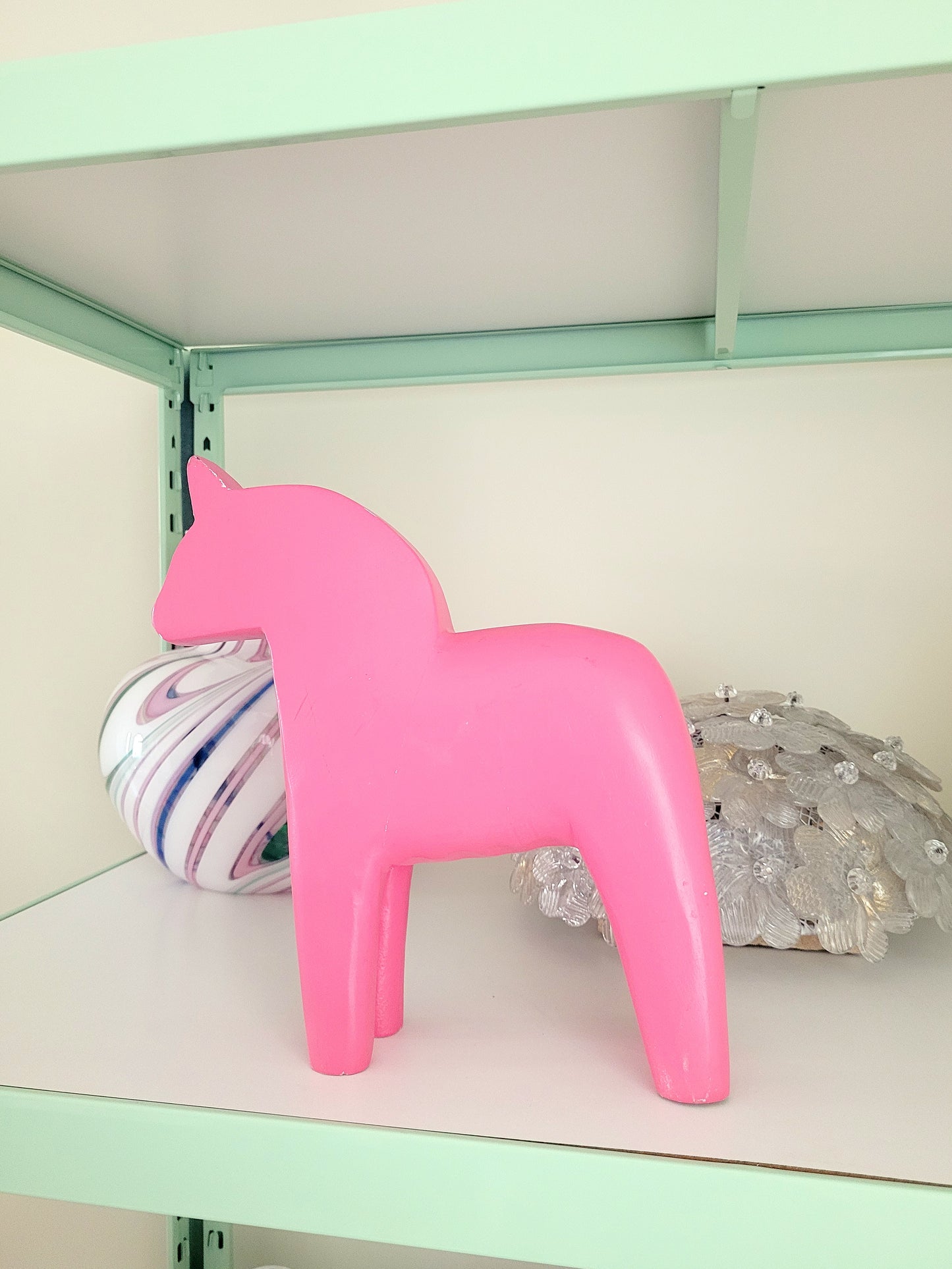 side view of a large pink wooden Dala horse on a shelf with other vintage items