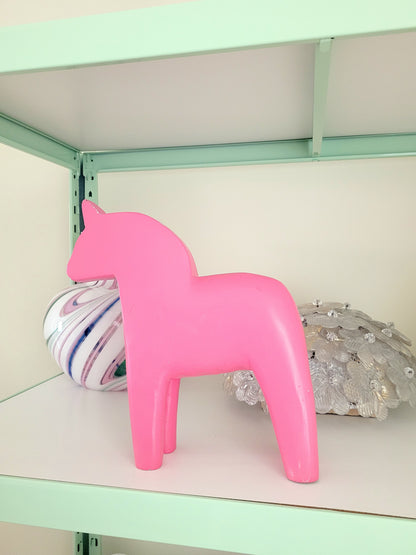 side view of a large pink wooden Dala horse on a shelf with other vintage items