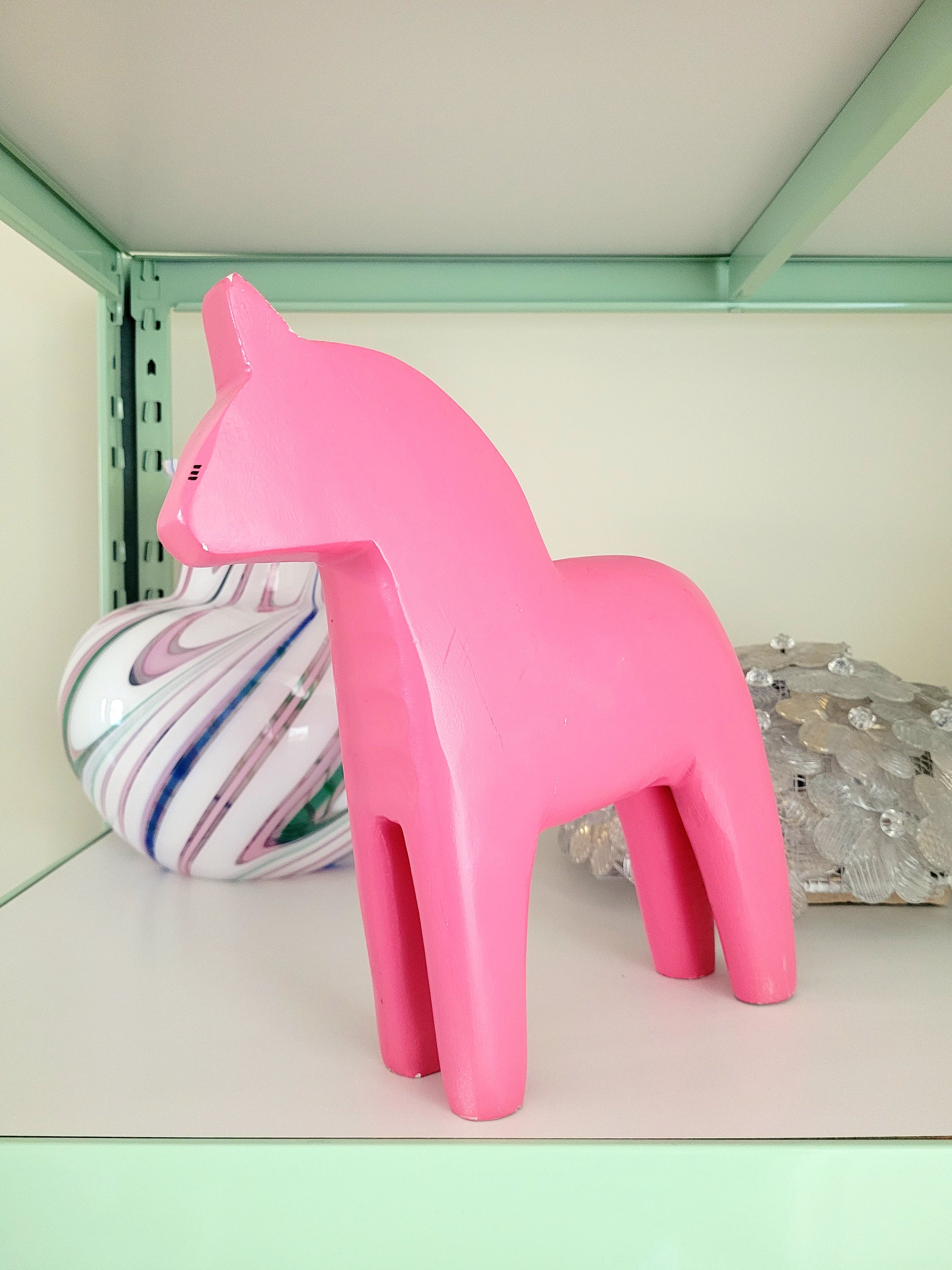 front view of a large pink wooden Dala horse on a shelf with other vintage items