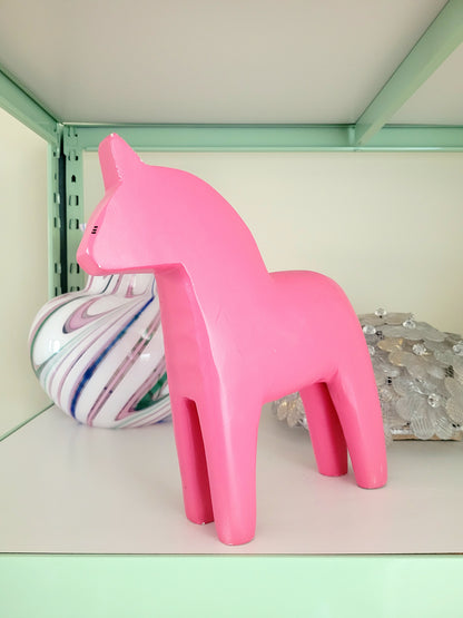 front view of a large pink wooden Dala horse on a shelf with other vintage items