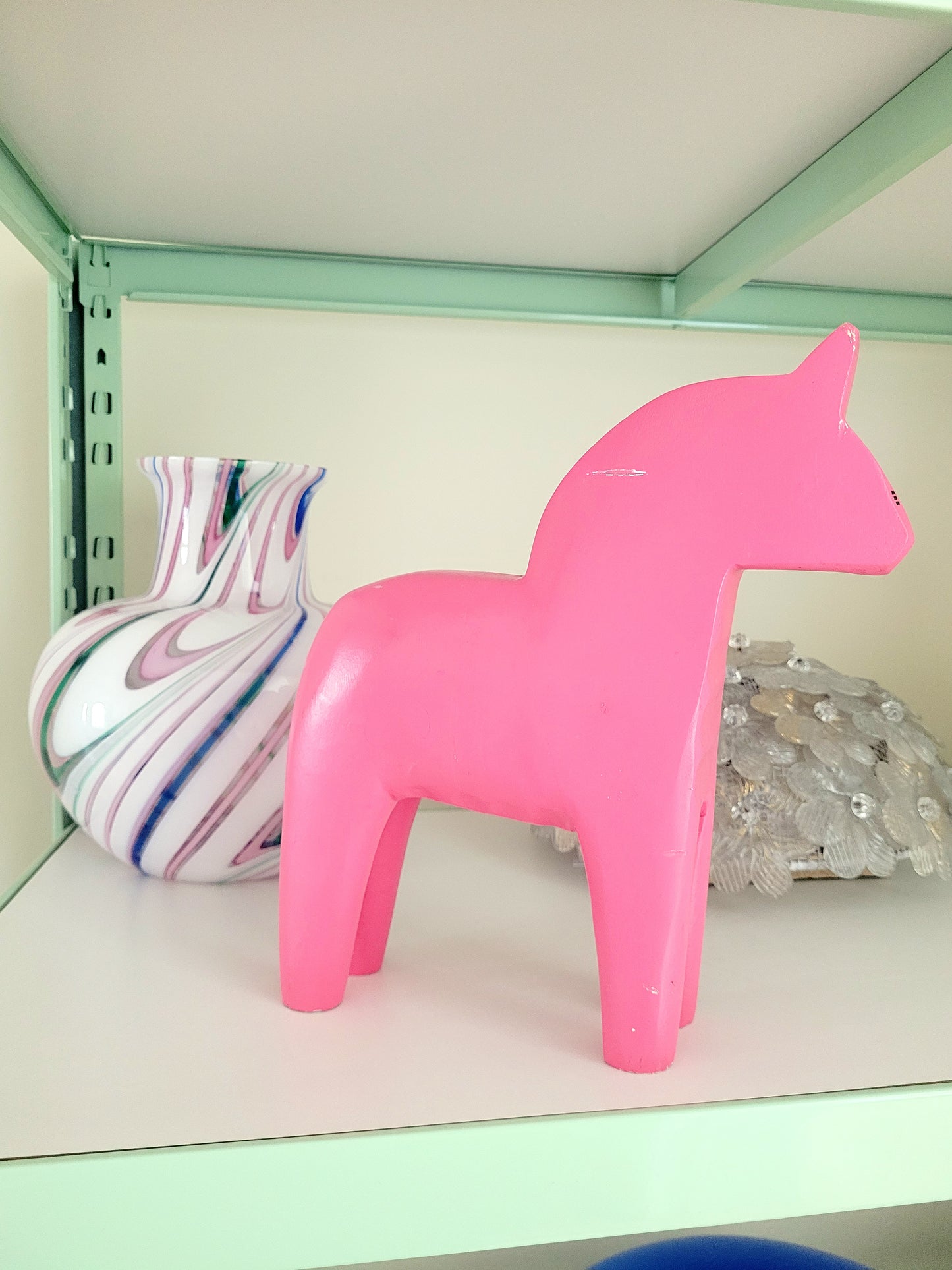 side view of a large pink wooden Dala horse on a shelf with other vintage items