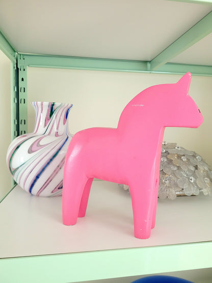 side view of a large pink wooden Dala horse on a shelf with other vintage items