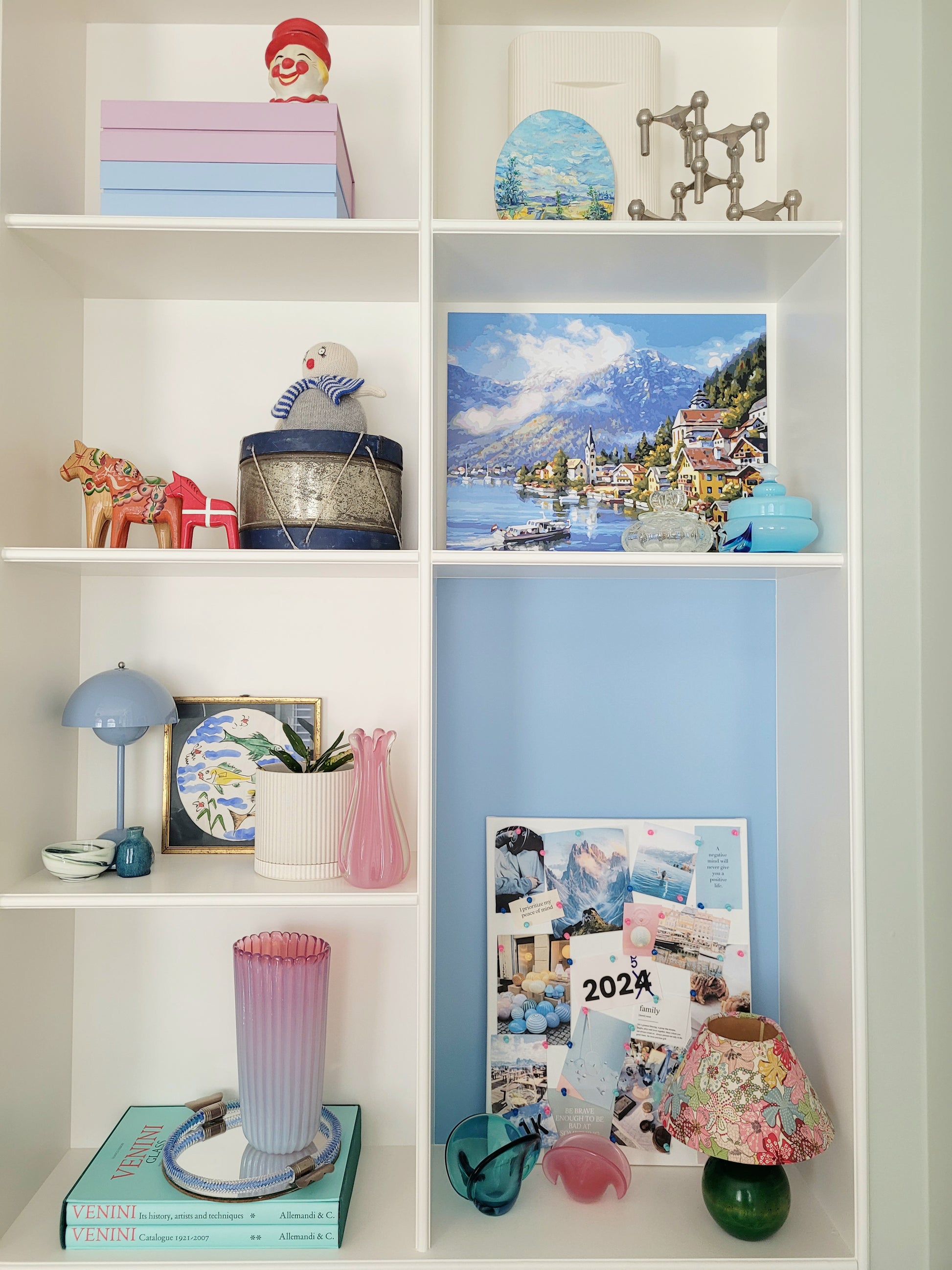 a large vintage pink ribbed Murano vase on a vintage Murano mirror tray and a stack of Venini books in a built-in cabinet full with vintage interior objects
