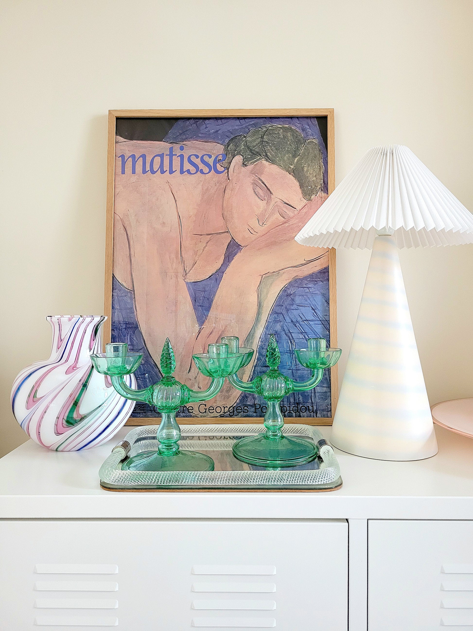 A pair of light green Murano glass candle holders, attributed to Vittorio Zecchin, renowned Italian artist on a vintage Murano mirror tray and with a Murano vase in the back and a framed Matisse poster.
