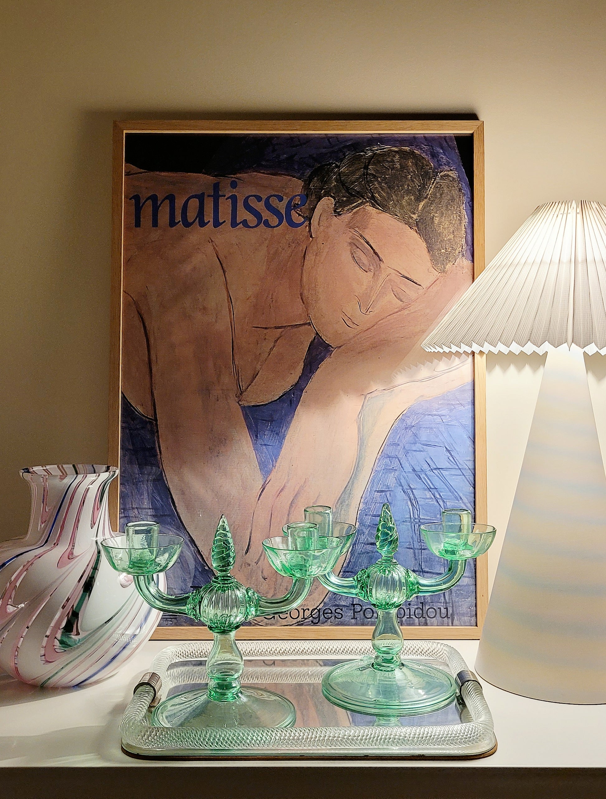 A pair of light green Murano glass candle holders, attributed to Vittorio Zecchin, renowned Italian artist on a vintage Murano mirror tray and with a Murano vase in the back and a framed Matisse poster.