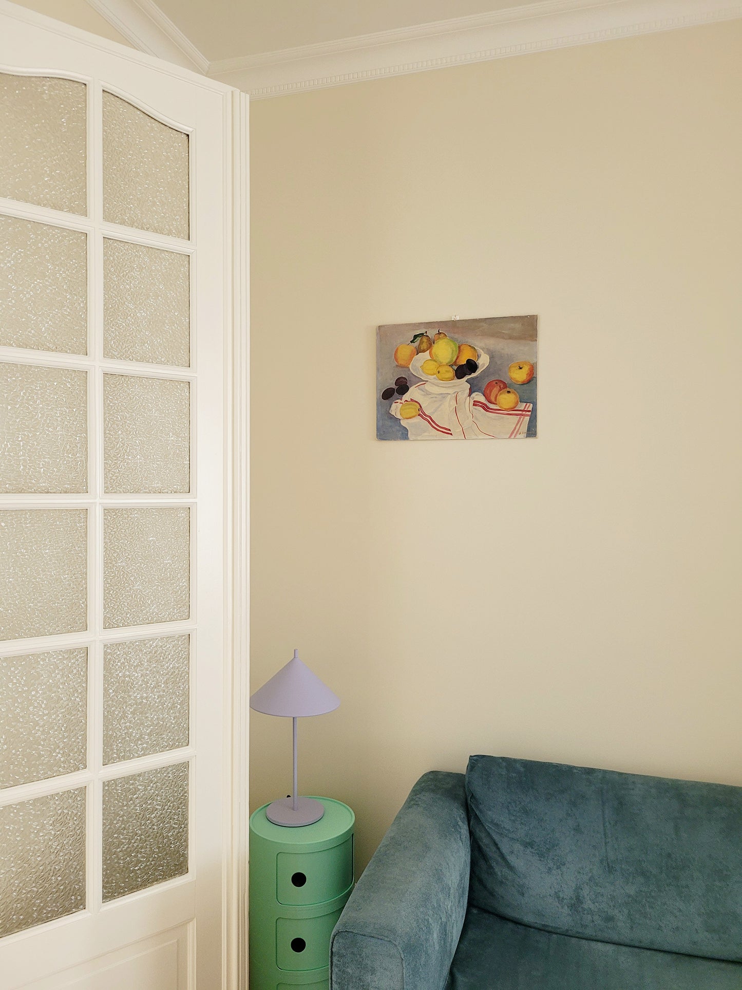 oil painting with still life of a fruit bowl on a  tea towel, hung on a yellow wall above a mint green side table with purple table lamp