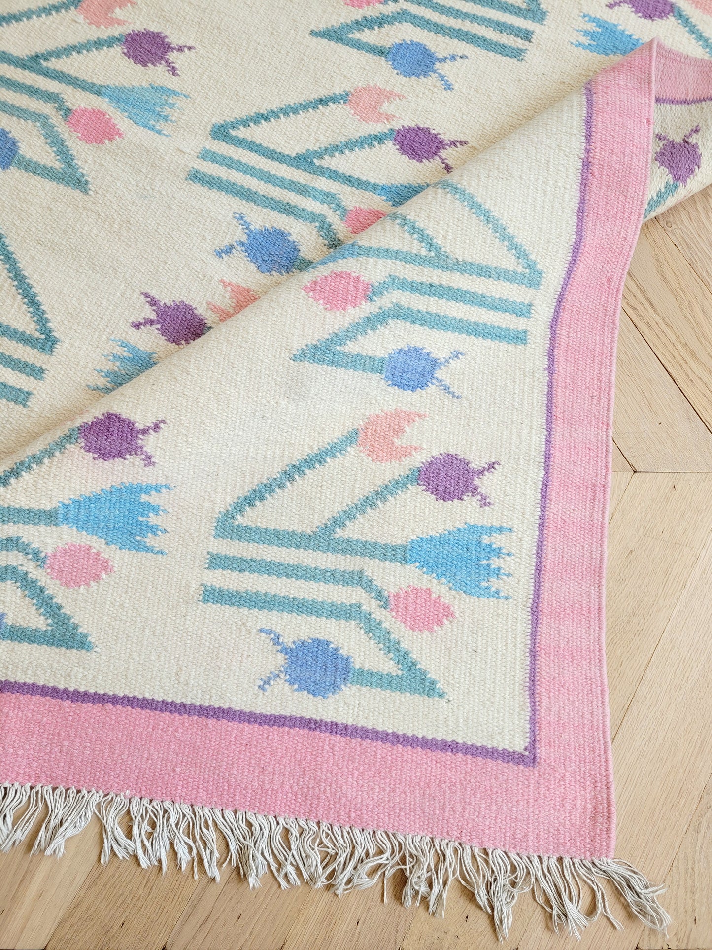 detailed top view of a pink and pastel coloured vintage rug with floral pattern