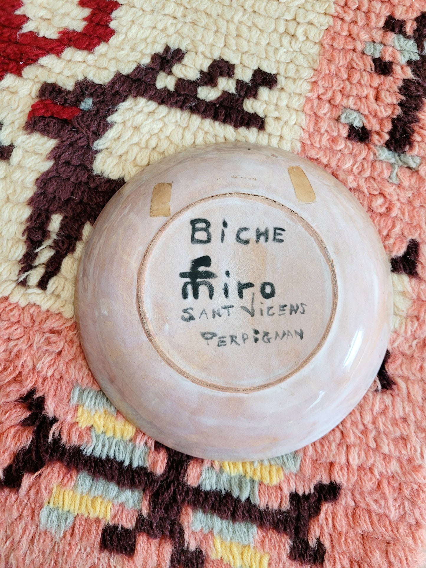back view of a small French wall plate depicting a doe and made by François Miro for Sant Vicens Ceramics, Perpignan, France. Blue and green colours. The plate is on a colourful rug.