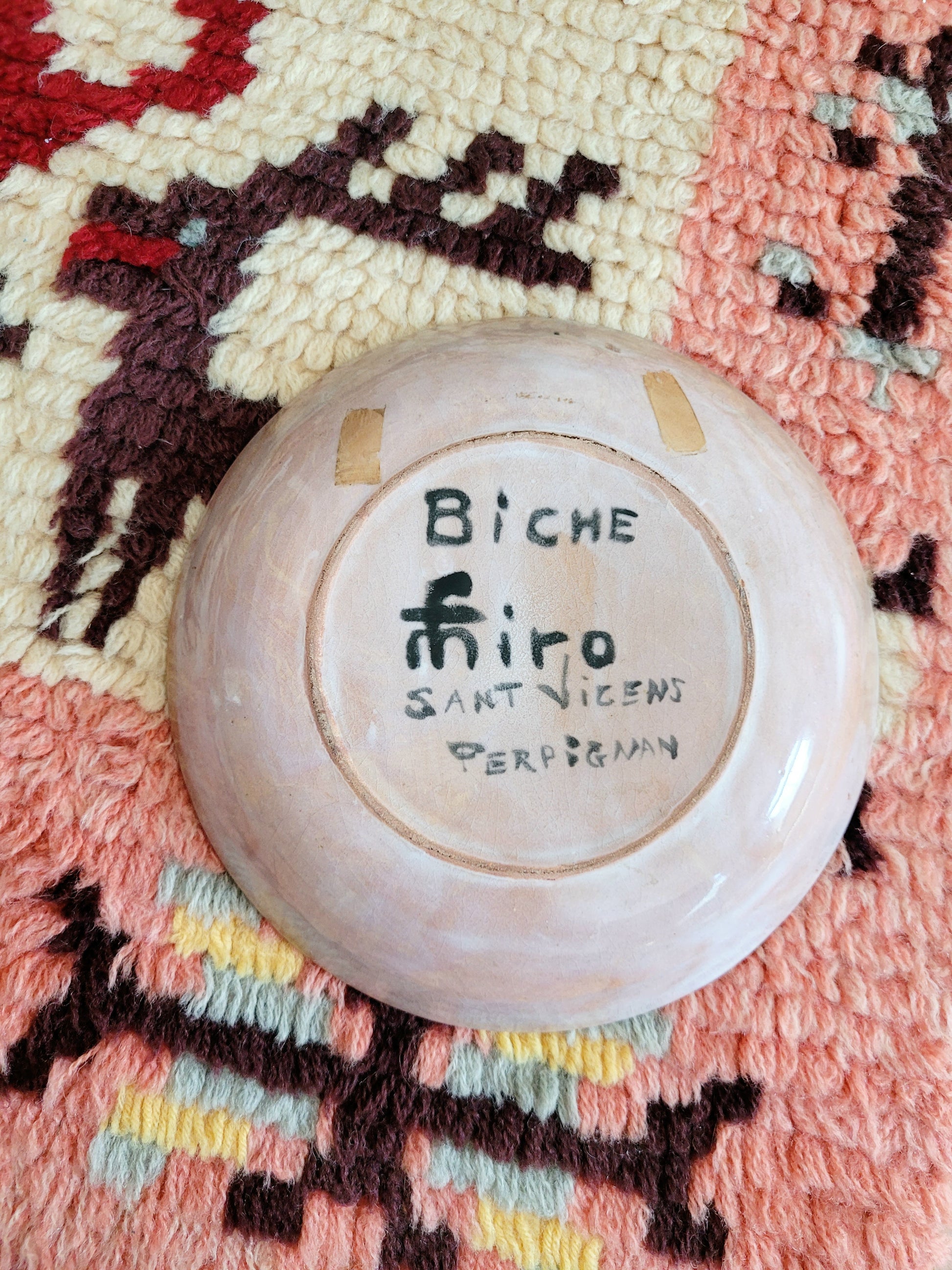 back view of a small French wall plate depicting a doe and made by François Miro for Sant Vicens Ceramics, Perpignan, France. Blue and green colours. The plate is on a colourful rug.