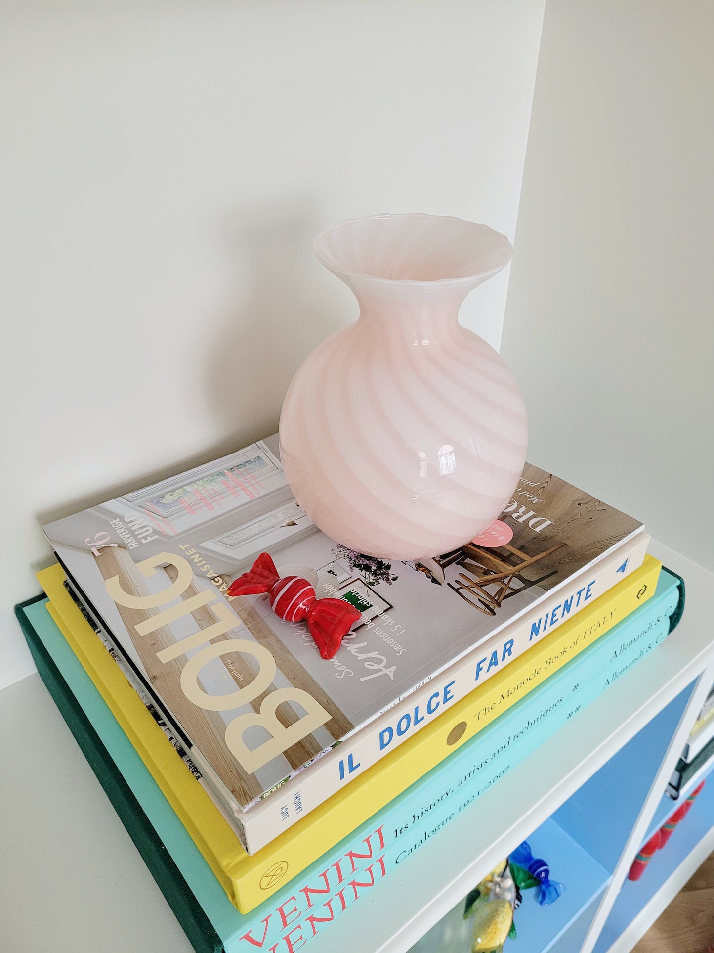 side view of a vintage Murano pink swirl vase on a stack of colourful books