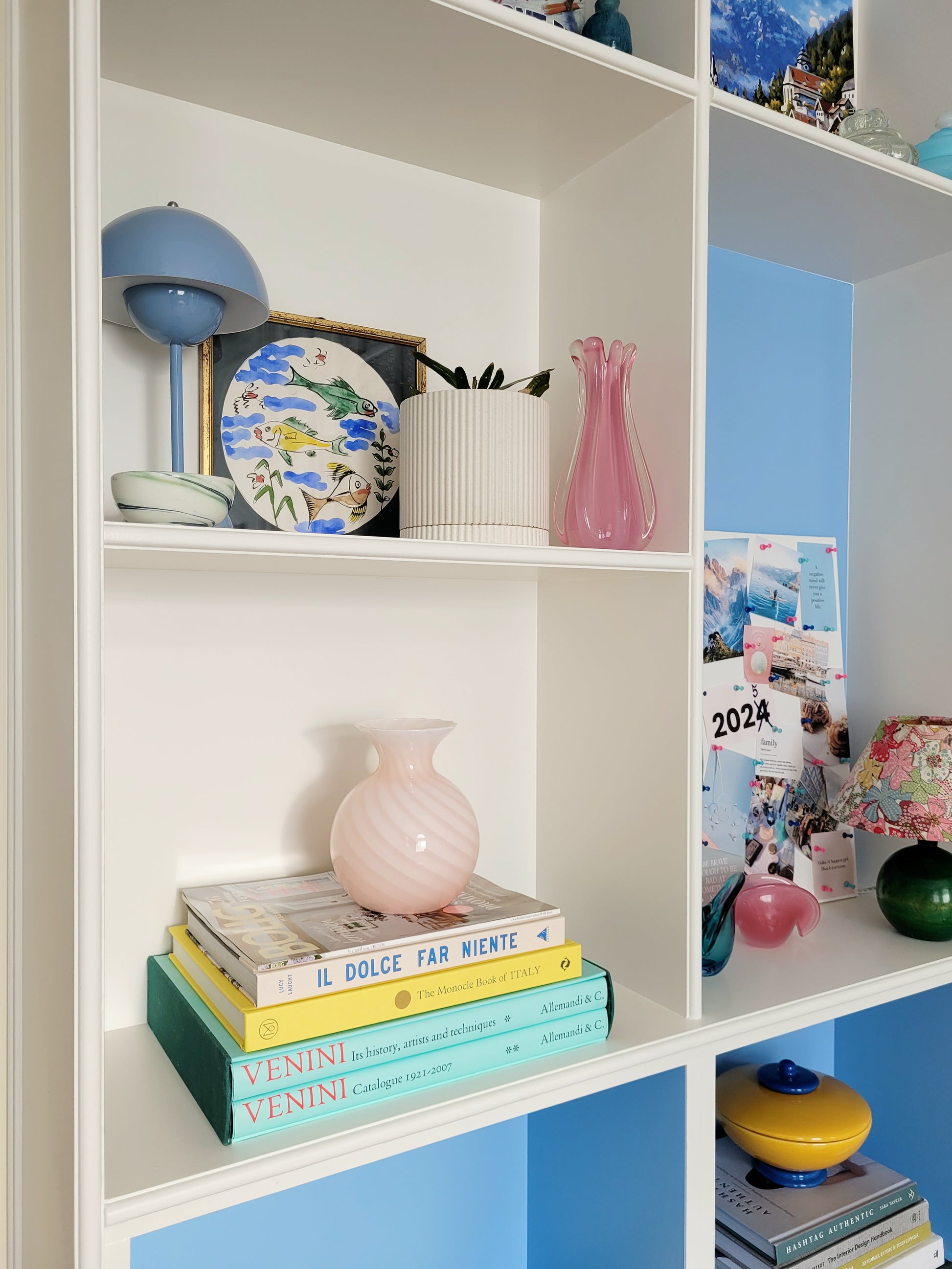 a vintage Murano pink swirl vase on a stack of colourful books in a built-in cabinet with vintage decor