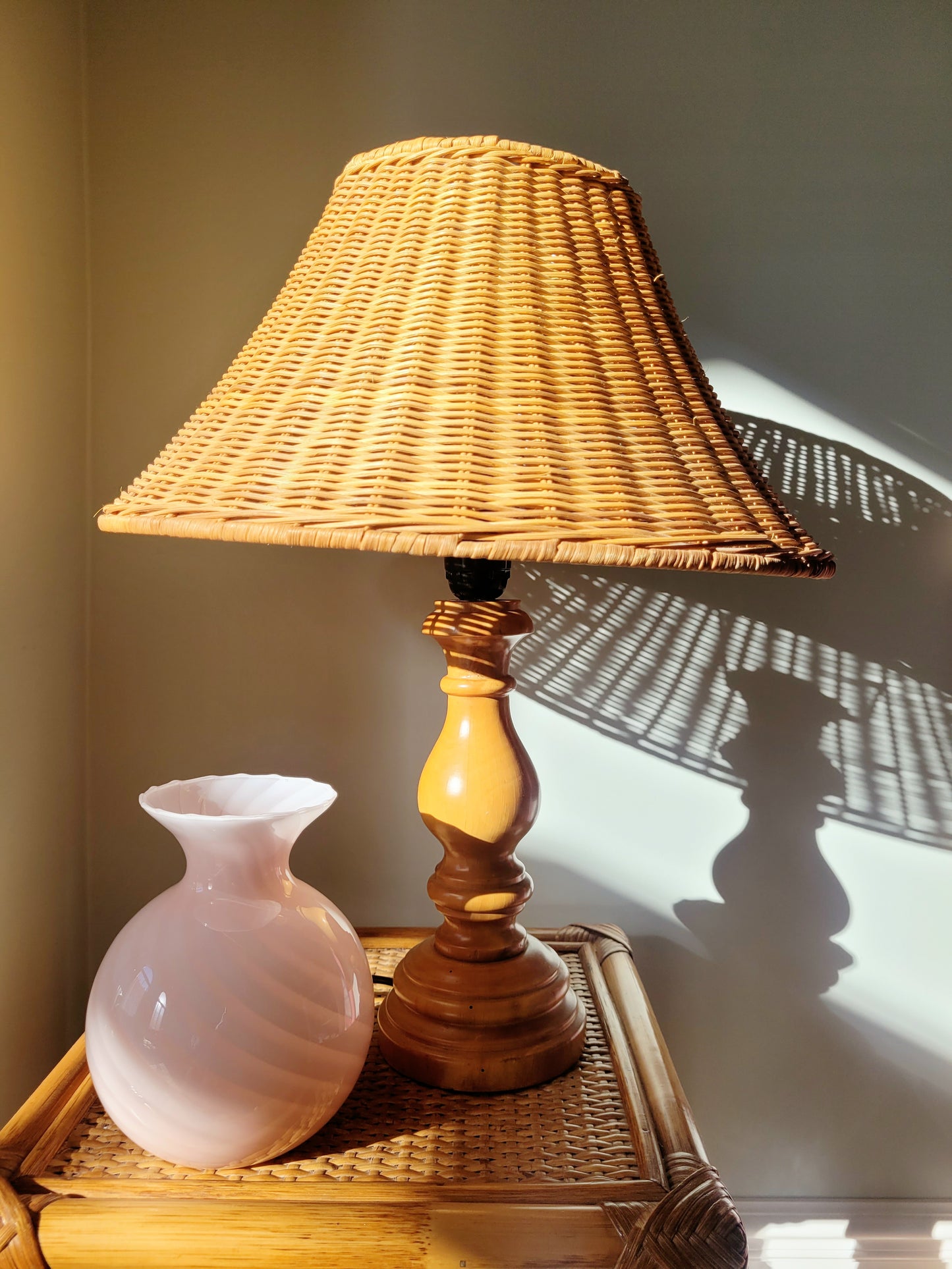 a vintage Murano pink swirl vase on a rattan side table next to a wood and rattan table lamp
