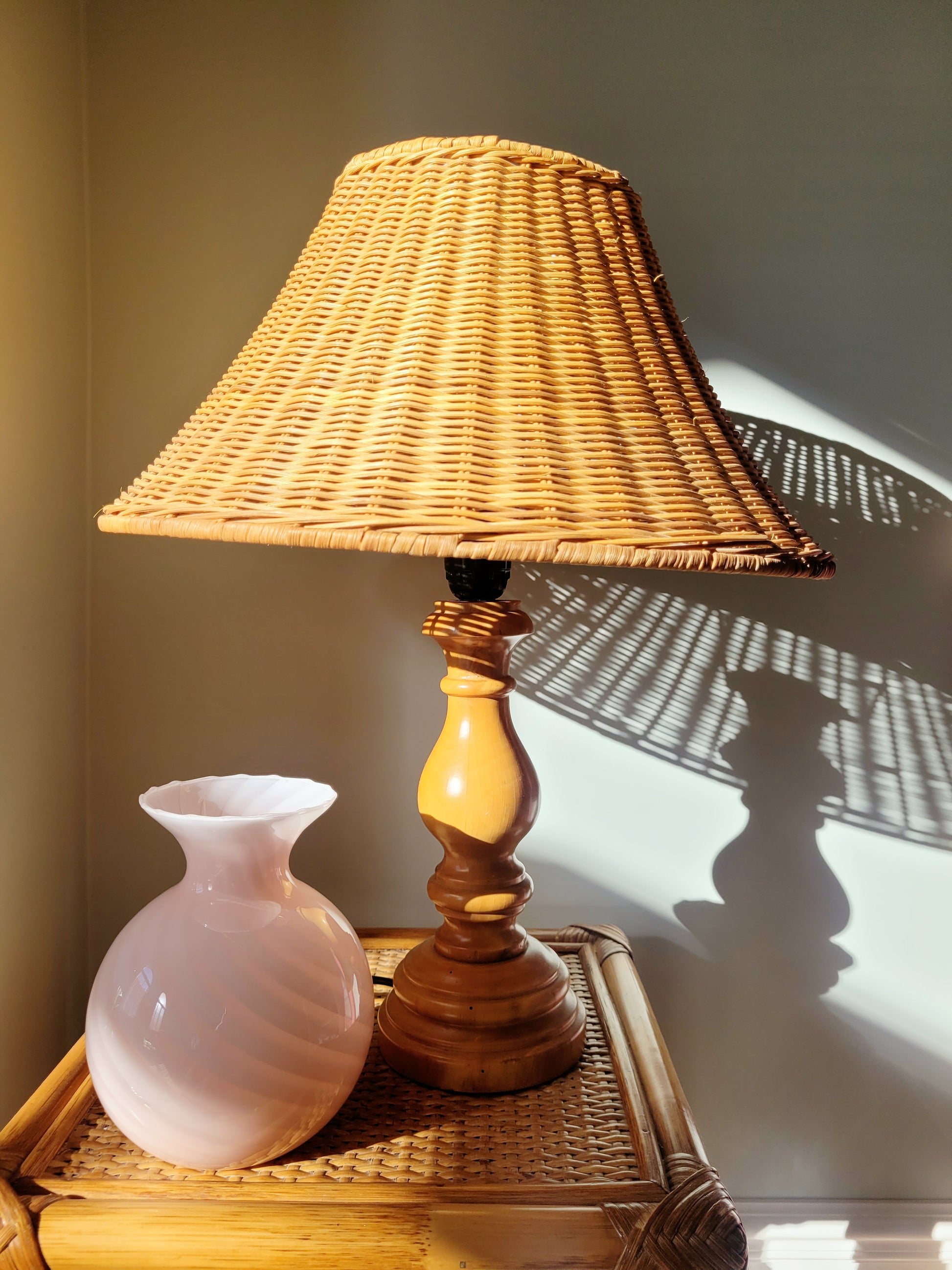a vintage Murano pink swirl vase on a rattan side table next to a wood and rattan table lamp