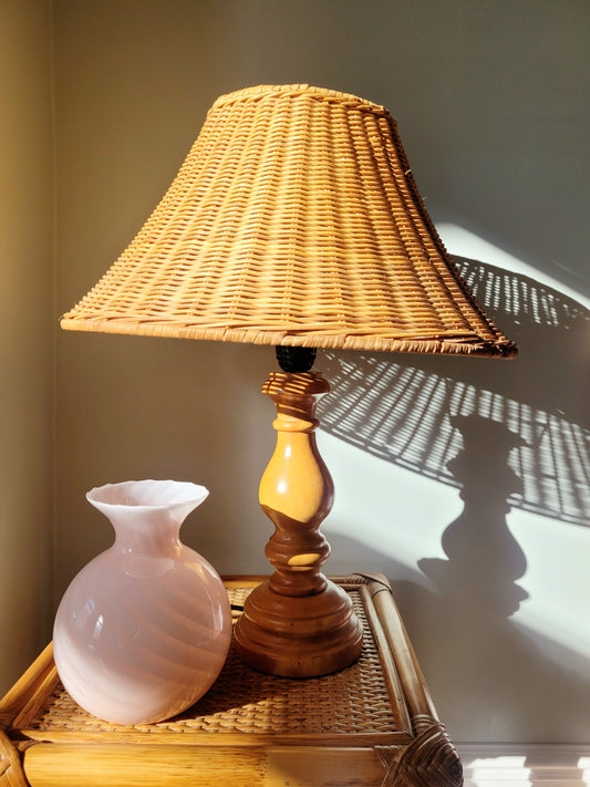 a vintage Murano pink swirl vase on a rattan side table next to a wood and rattan table lamp