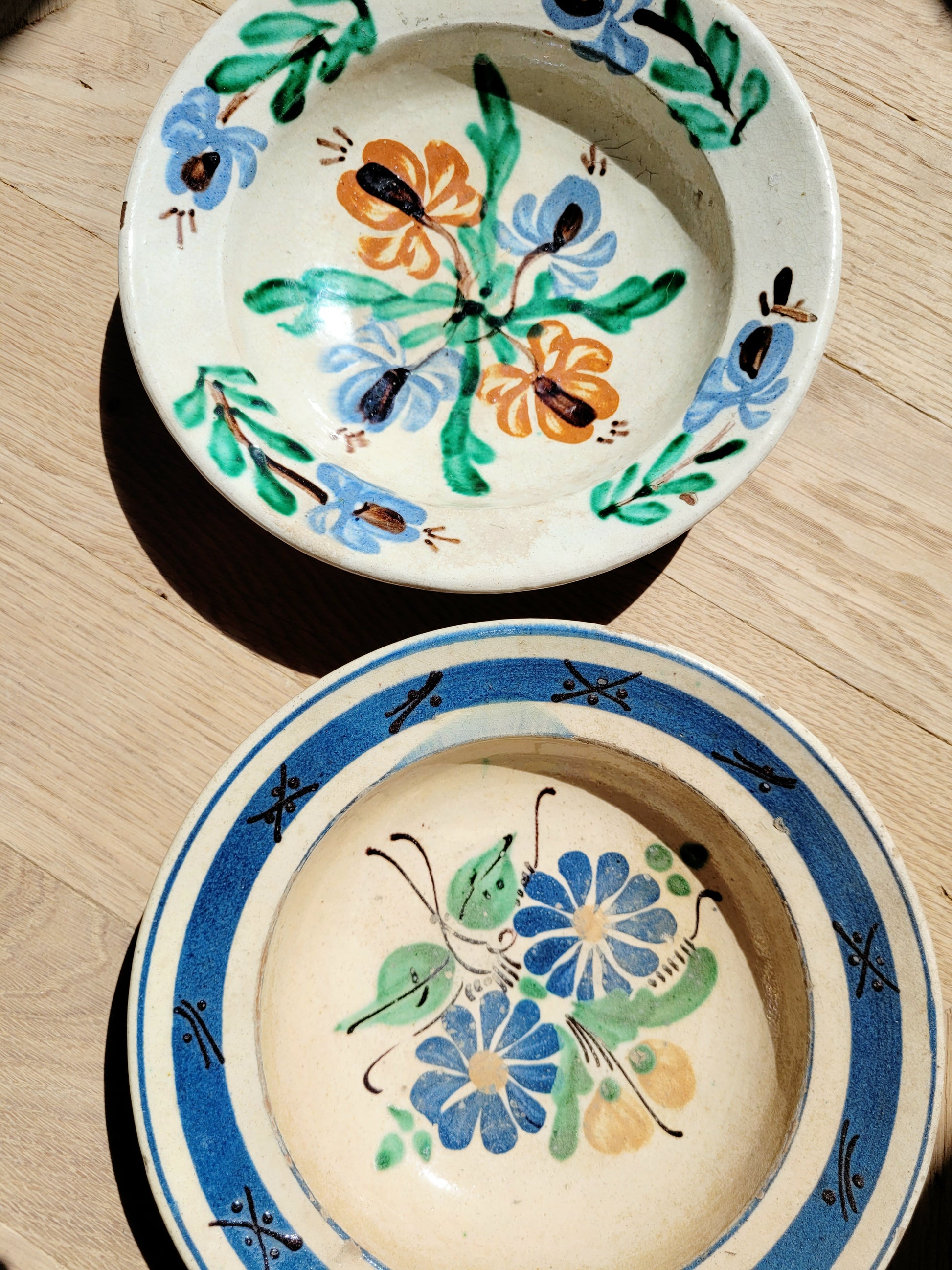 detail of two vintage hand-painted earthenware wall plates/bowls from Romania-Hungary with floral design on a parquet floor, typical folk art