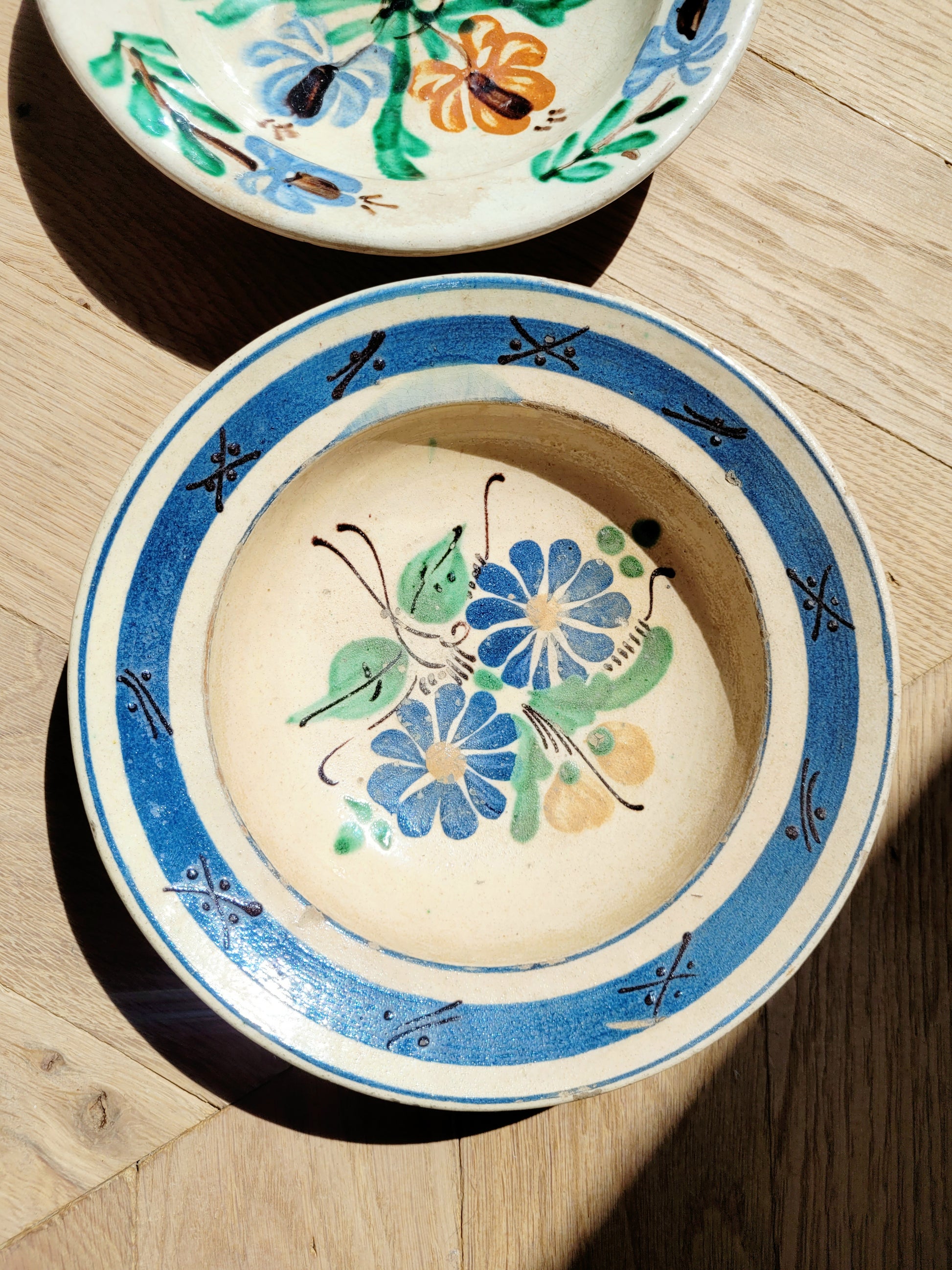 detail of a vintage hand-painted earthenware wall plate/bowl from Romania-Hungary with floral design on a parquet floor, typical folk art