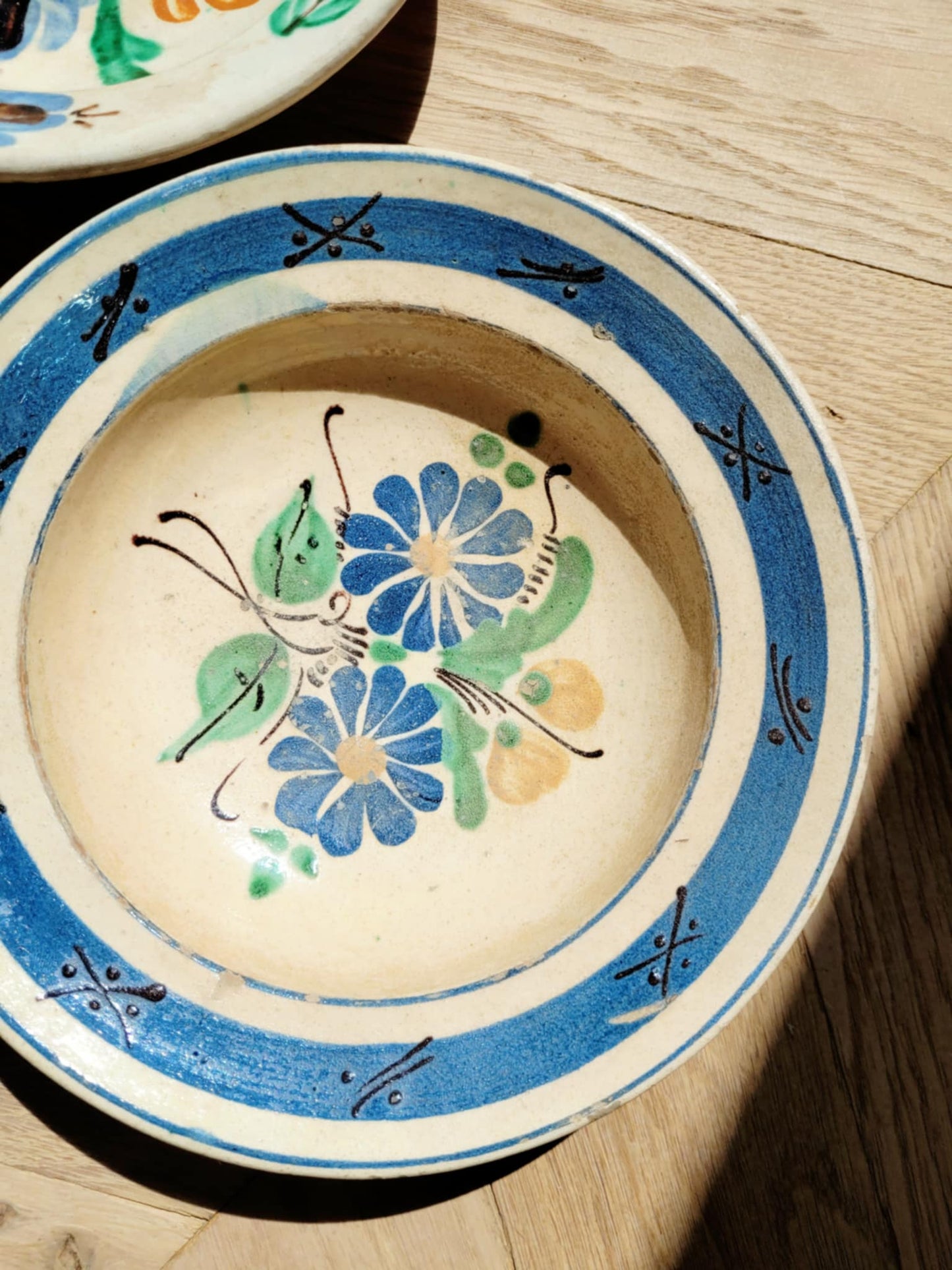 vintage hand-painted earthenware wall plate/bowl from Romania-Hungary with floral design on a parquet floor, typical folk art